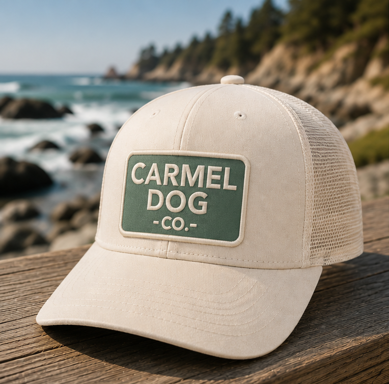 Beige trucker hat with 'Carmel Dog Co.' logo, shown from multiple angles with a coastal background.